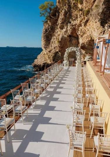 White ceremony chairs on a deck at the foot of a cliff beside the sea on the Albanian Riviera