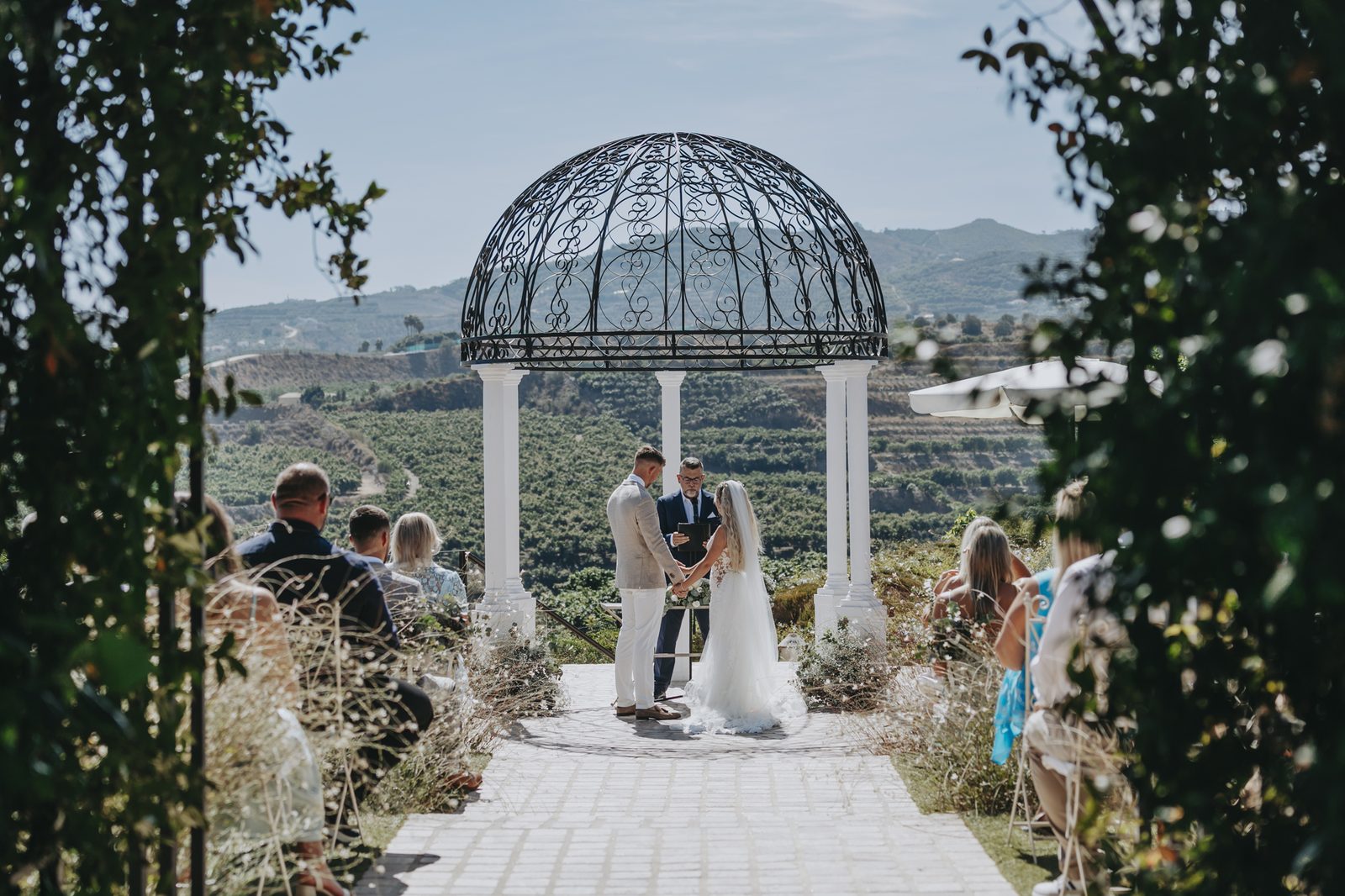 A couple saying their vows under an ironwork gazebo looking out over the hills of Andalusia