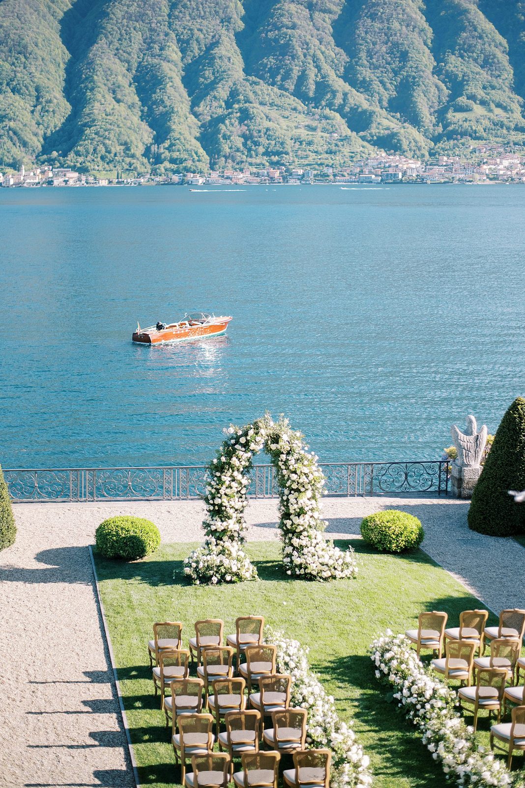 Wedding ceremony set up on a lakeside terrace at Lake Como, with a wooden boat on the water and the hills behind