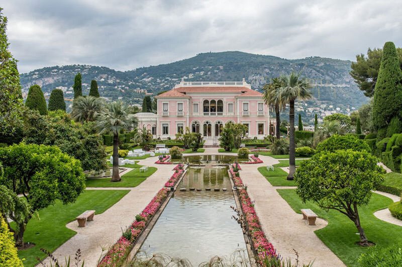 A pink villa on the French Riviera with formal gardens and a long pool leading up to it